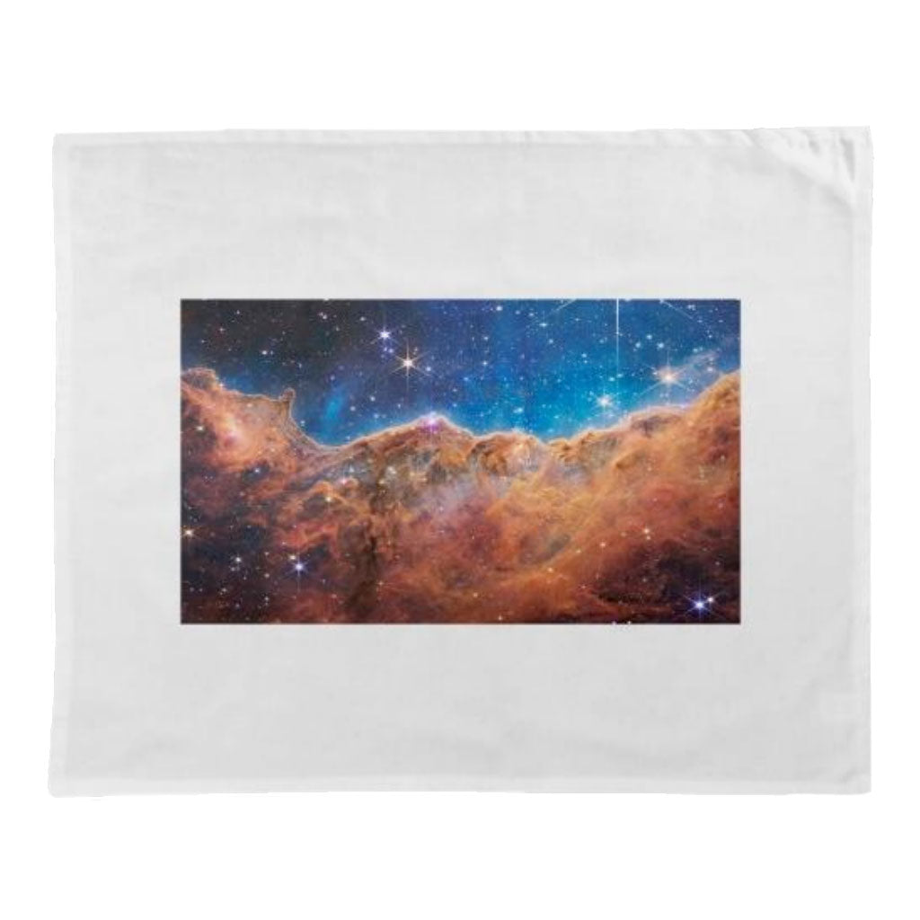 The James Webb Space Telescope Carina Nebula Tea Towel features a stunning image of the colorful Carina Nebula, with glowing stars, blue and orange gas clouds, and a dark cosmic background on a white cloth.