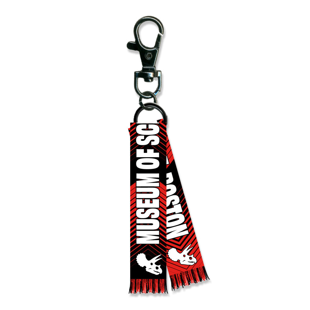 The Museum of Science Boston World Cup Scarf Keychain is a black keychain with a lobster clasp and a red and black tag reading “Museum of Science Boston” in bold white letters, featuring dinosaur skull graphics and red fringe.