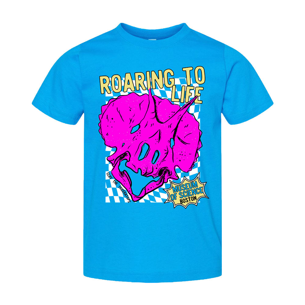 The Museum of Science Boston Roaring Toddler T-Shirt features a bright blue design with a large pink triceratops skull graphic, bold text that says “Roaring To Life,” and a comic-style caption. Set against a blue-and-white checkered background, this fun educational kids’ shirt is perfect for aspiring paleontologists!.