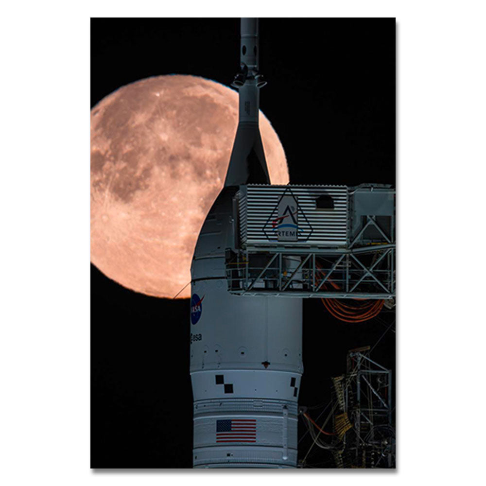 A NASA Artemis rocket stands on a launch pad at night, with a large, bright full moon rising in the background. The American flag and Artemis logo are visible on the rocket, creating the perfect inspiration for the Artemis Full Moon Lenticular Magnet—a unique lunar keepsake and thoughtful space gift for any astronomy enthusiast.