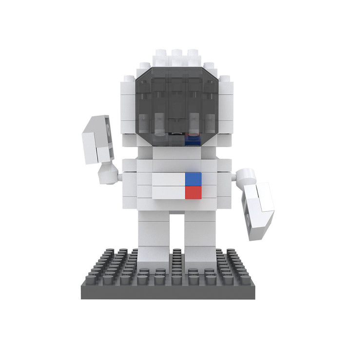 A small astronaut figure constructed from white Space Mystery Mini Blocks stands on a black base, featuring a dark helmet visor and red and blue square details on its chest—a collectible set designed to inspire creativity and problem-solving skills.