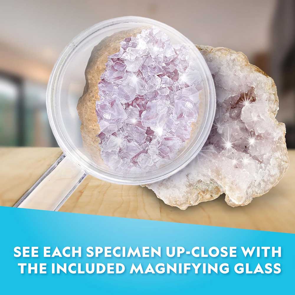 A magnifying glass reveals a detailed view of a light purple crystal geode resting on a wooden surface. Text below reads, See each specimen up-close with the included magnifying glass—perfect for exploring your Outer Space Dig Kit or any educational science kit.